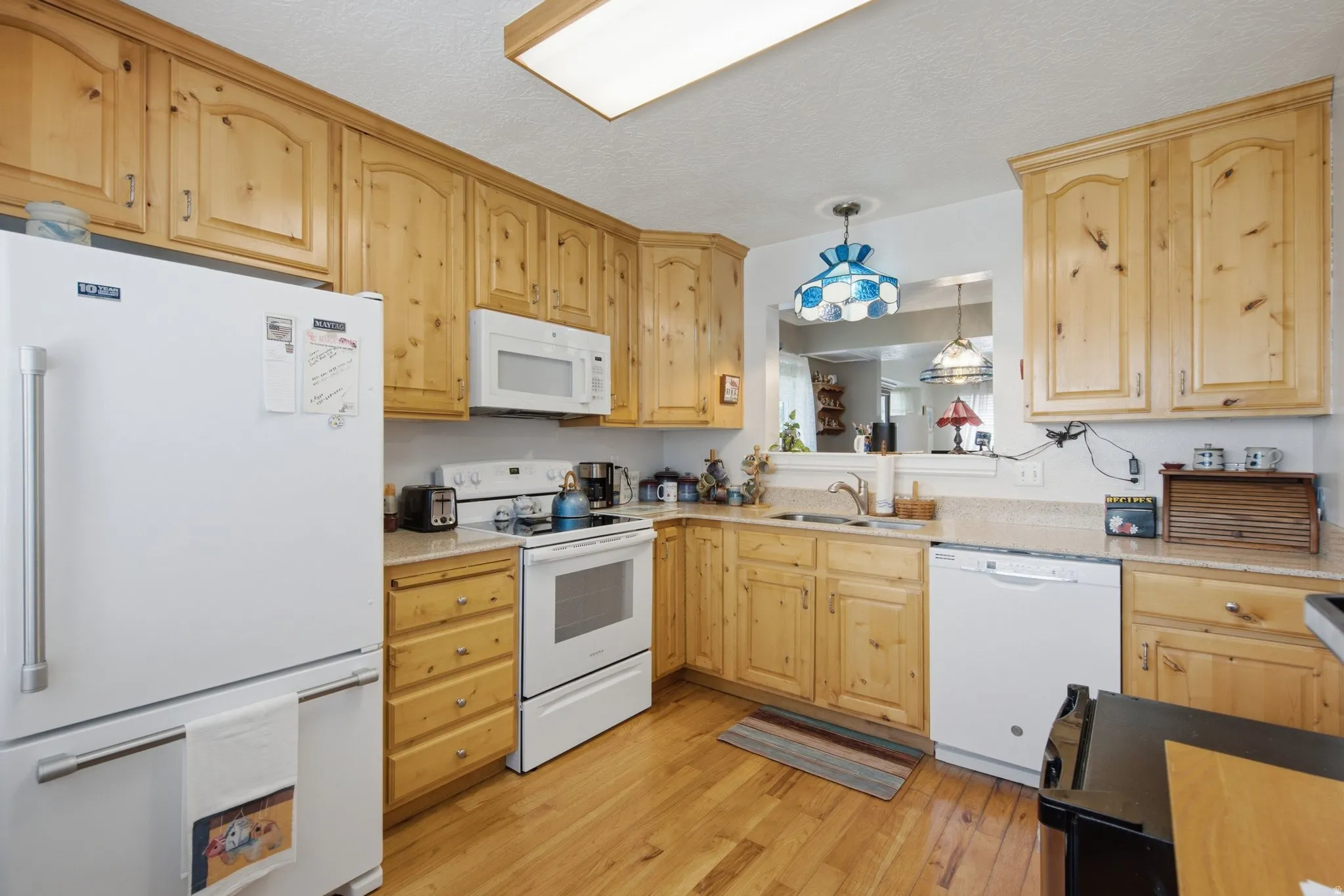 Kitchen featuring light wood cabinetry, light wood-finish flooring, white appliances, a pass-through window, and a recessed ceiling light