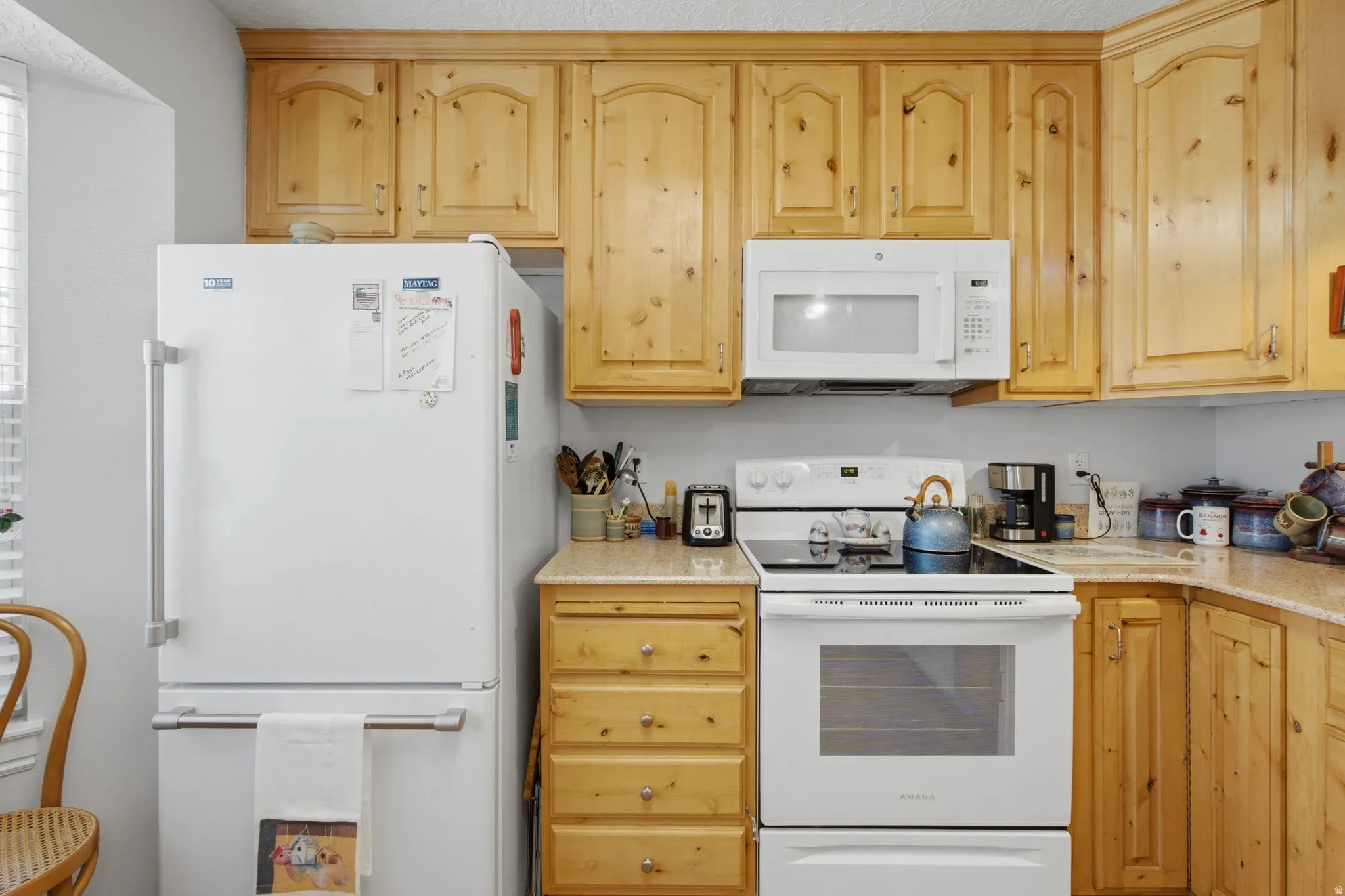 Kitchen featuring wood-finish cabinetry, light-toned countertops, and a white appliance suite including a range and microwave