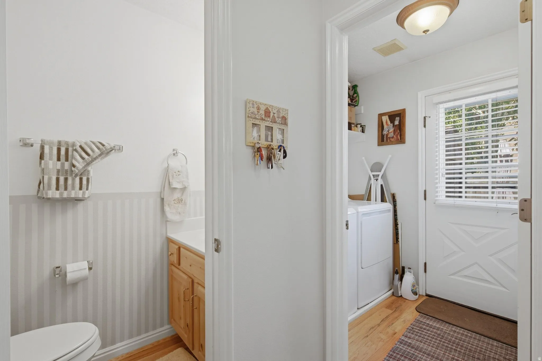 Utility area featuring a white paneled door with horizontal blinds, wood-finish flooring, and a flush mount light fixture