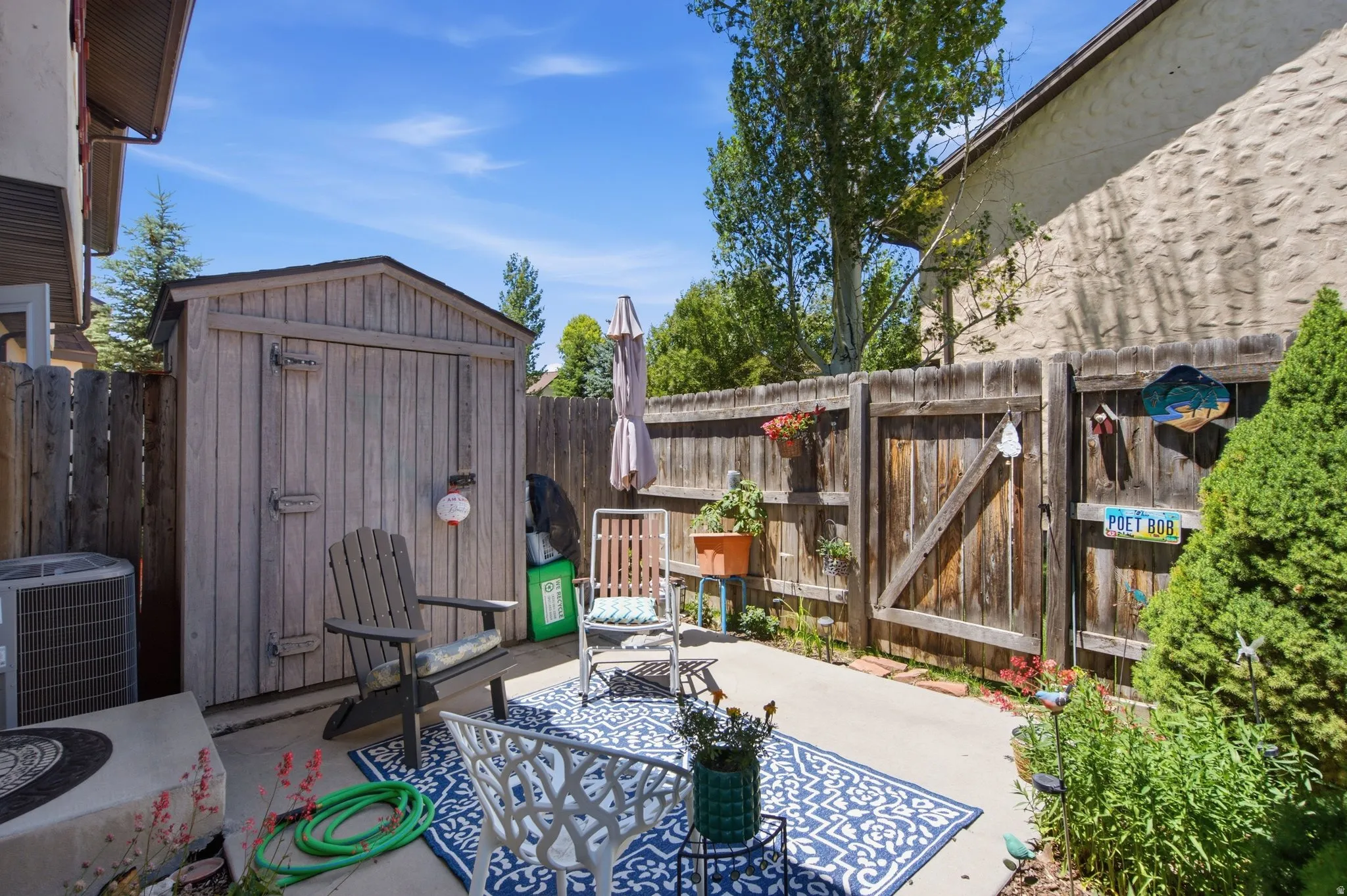Private patio space featuring a storage shed with double doors, wood fencing, concrete paving, and an outdoor air conditioning unit