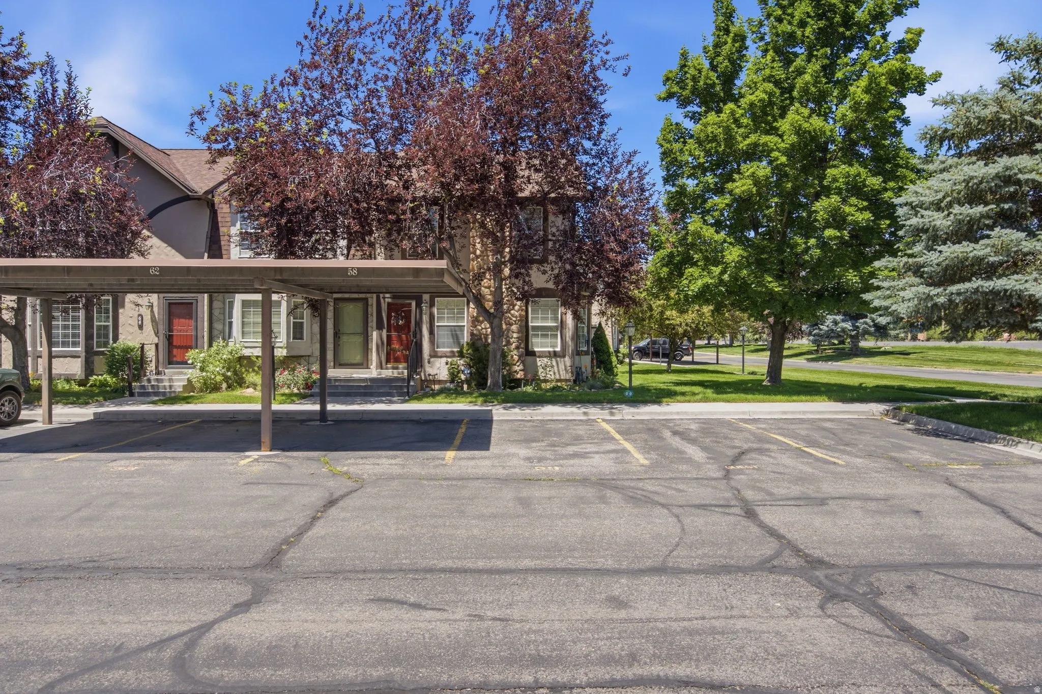 Exterior of multi-unit property featuring a carport, mature trees, and a paved parking area