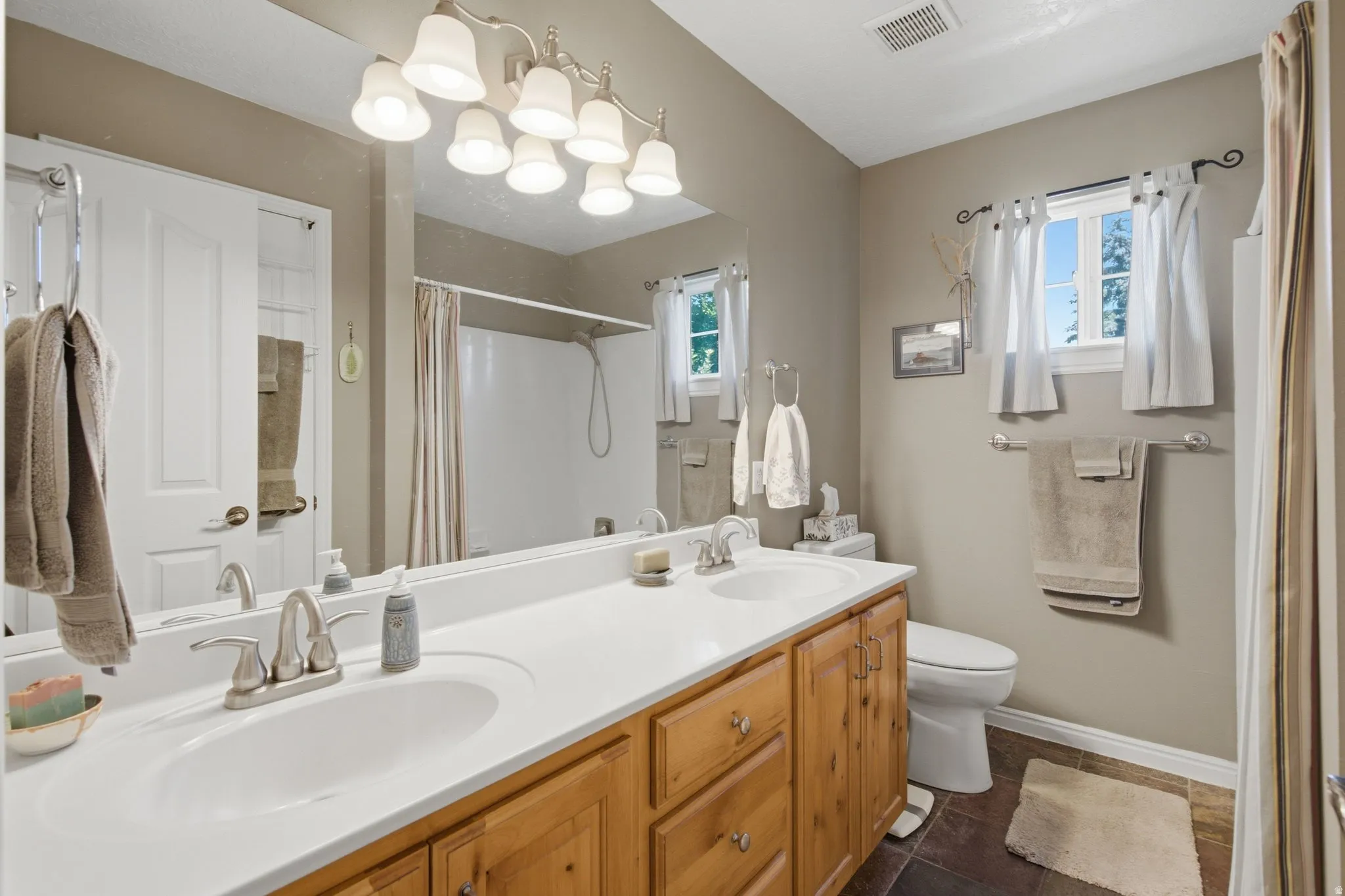 Double vanity with white integrated sinks, light wood-finish cabinetry, and brushed nickel fixtures