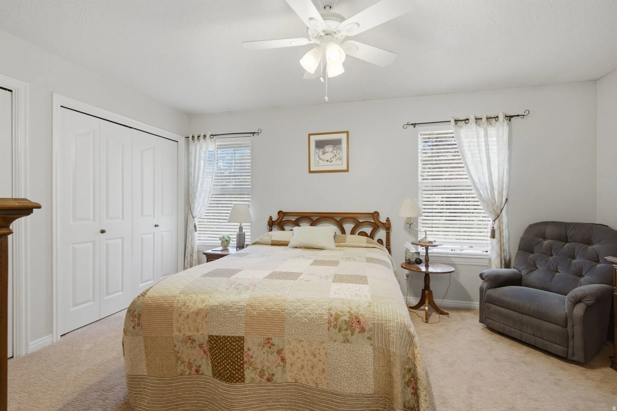 Carpeted bedroom featuring a ceiling fan, two windows with blinds, and white bifold closet doors