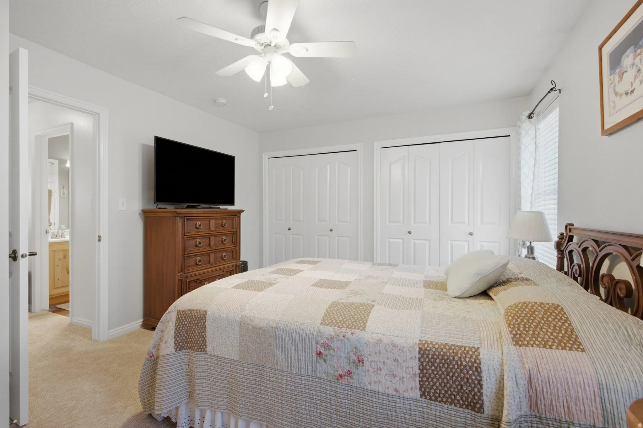 Carpeted bedroom with a ceiling fan, dual bi-fold closet doors, and a window with blinds