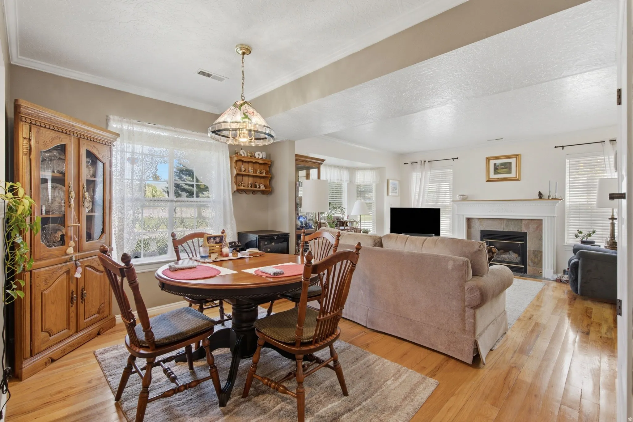 Open-concept dining area with wood-finish flooring, featuring a decorative chandelier and natural light from a large window