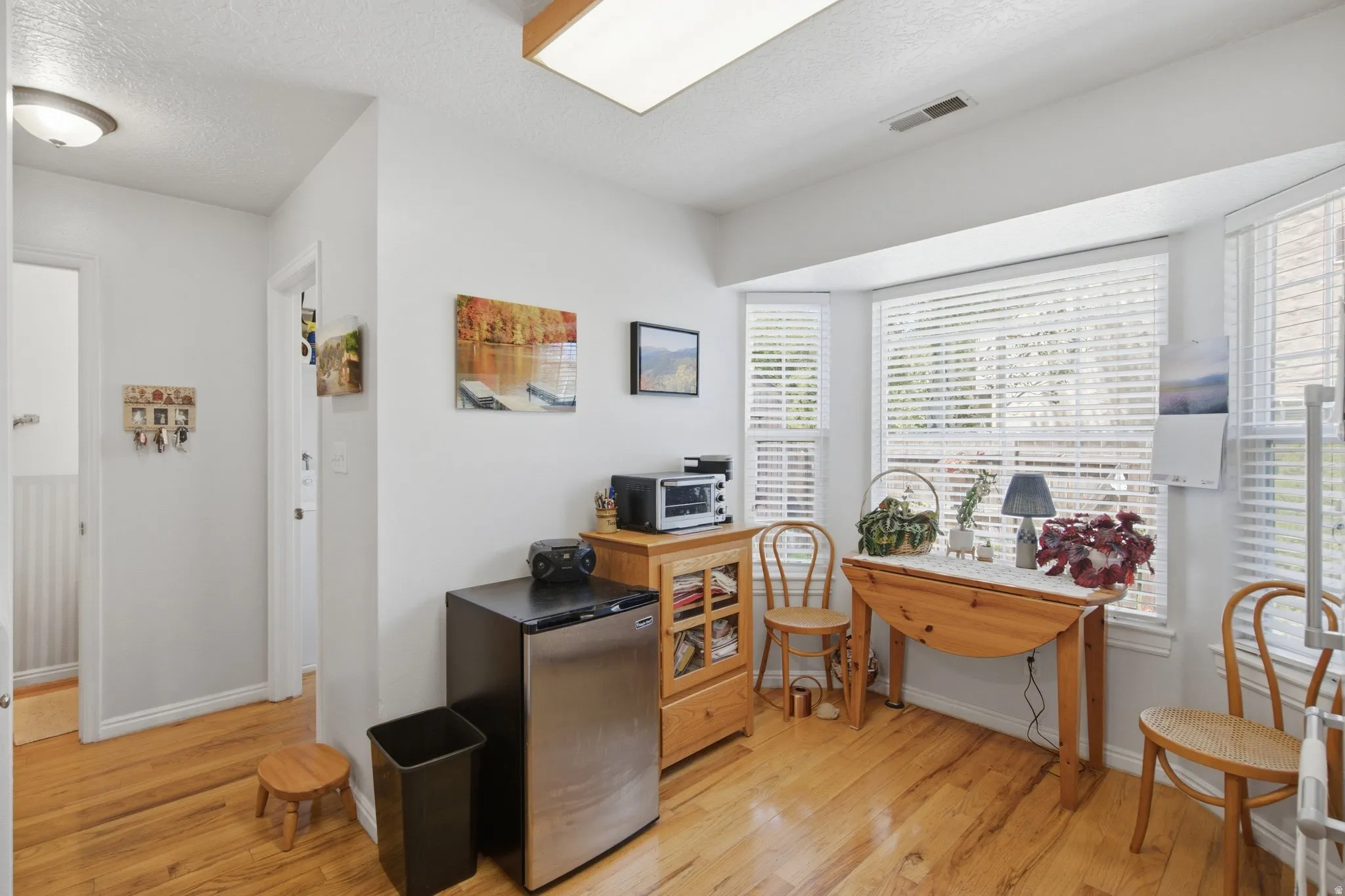 Bay window with white blinds, wood-finish flooring, and light neutral wall paint