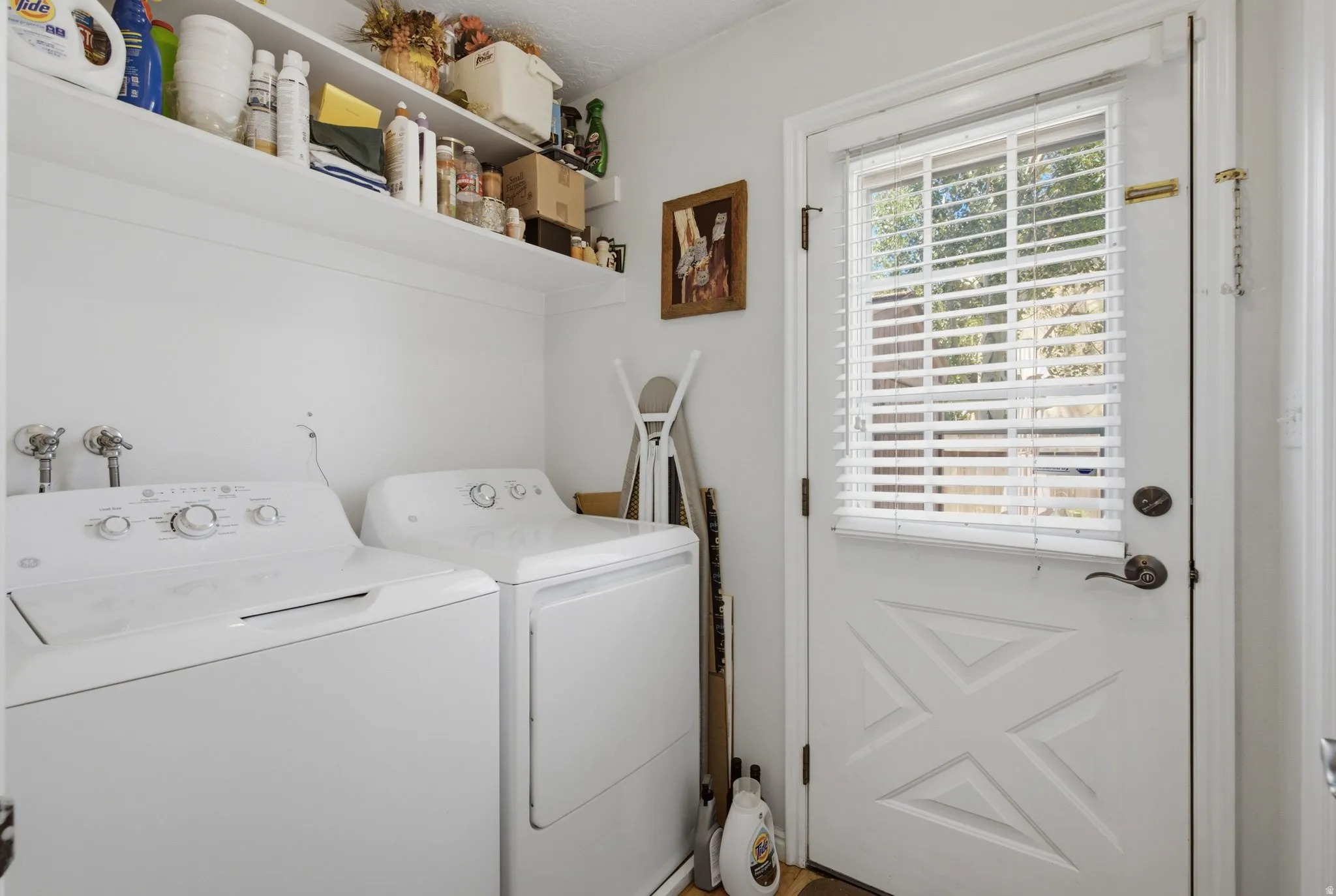 Dedicated laundry area featuring a white door with window and blinds, white walls, and built-in shelving