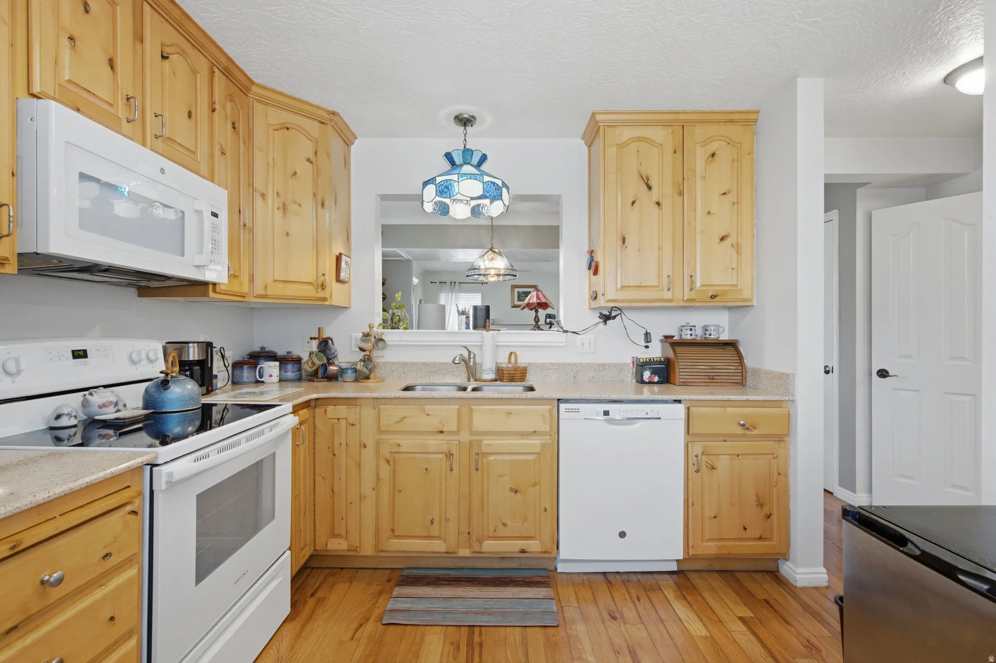 Kitchen featuring wood-finish flooring, wood cabinetry, stone-look countertops, and white appliances including a microwave, range, and dishwasher
