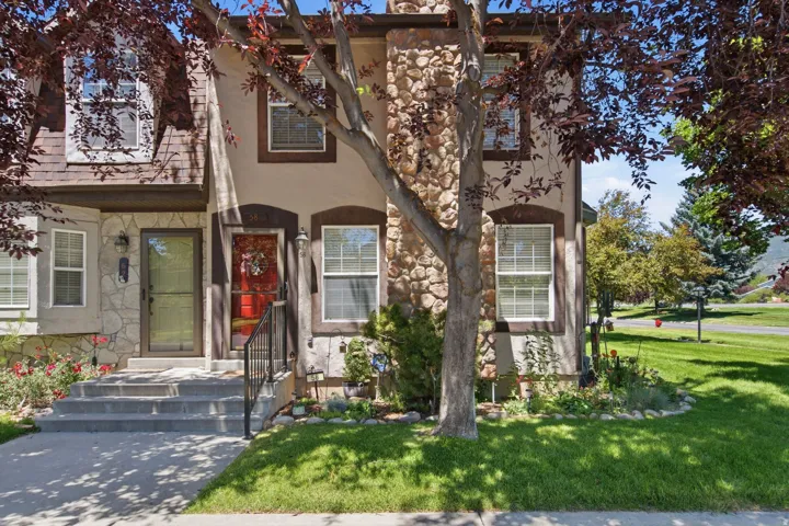 Two-story stucco and stone exterior featuring a red entry door, white-framed windows with dark trim, an asphalt shingle roof, and a stone chimney