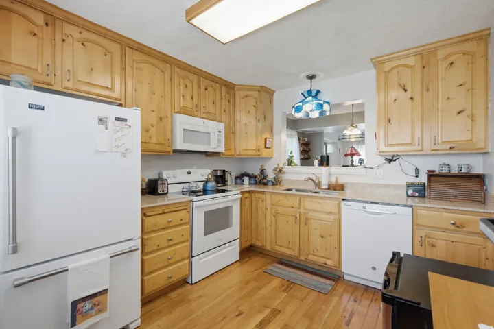 Kitchen featuring light wood cabinetry, light wood-finish flooring, white appliances, a pass-through window, and a recessed ceiling light