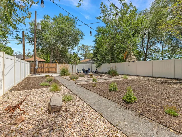 Private backyard with white vinyl fencing, a gravel pathway, and dedicated garden beds