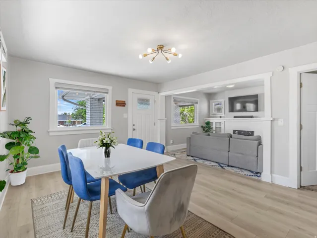 Open-concept living and dining area featuring light wood-finish flooring, a contemporary chandelier, and a bright white front door with glass inlay