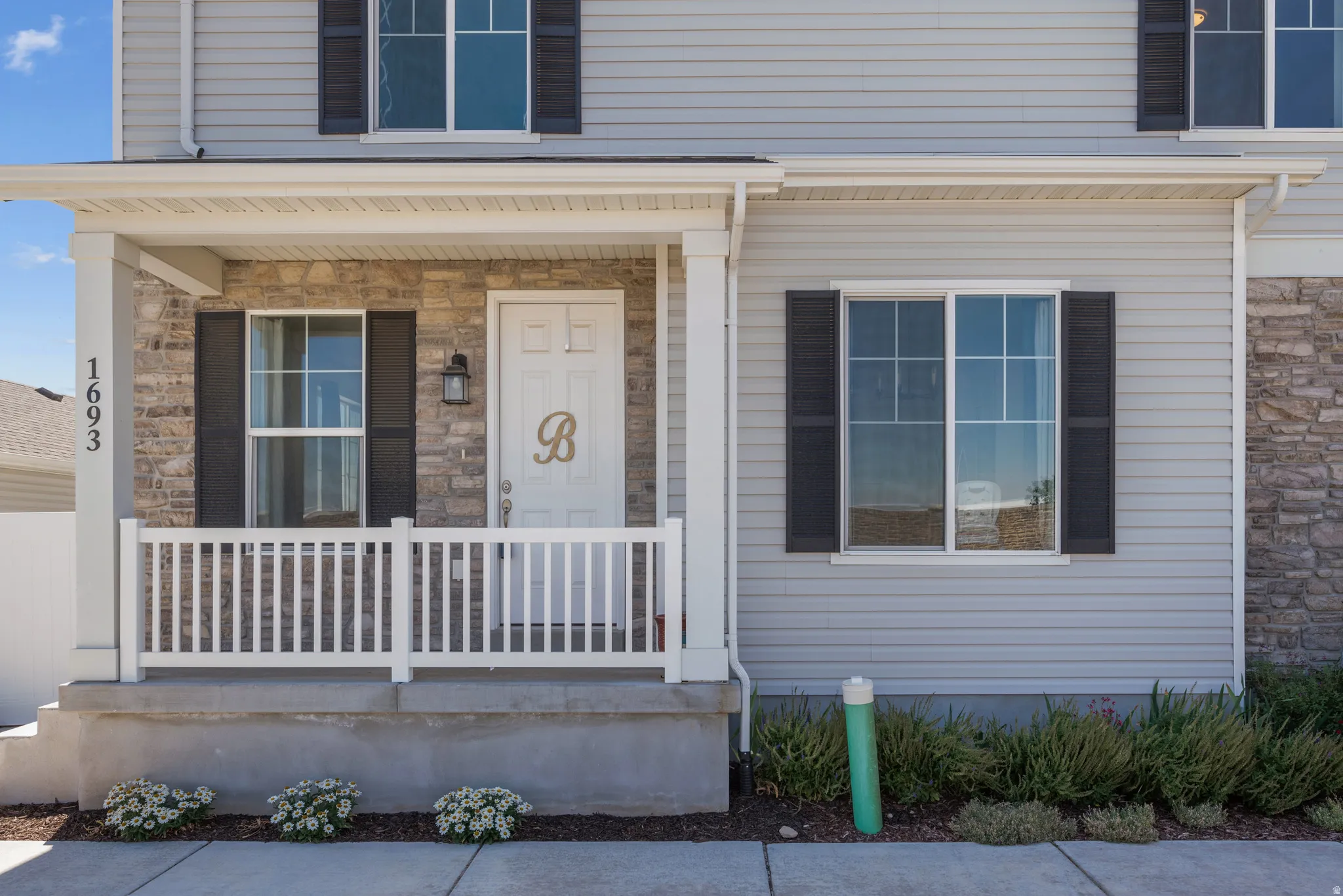 Covered porch entry featuring stone accent siding, light gray horizontal siding, and black exterior shutters