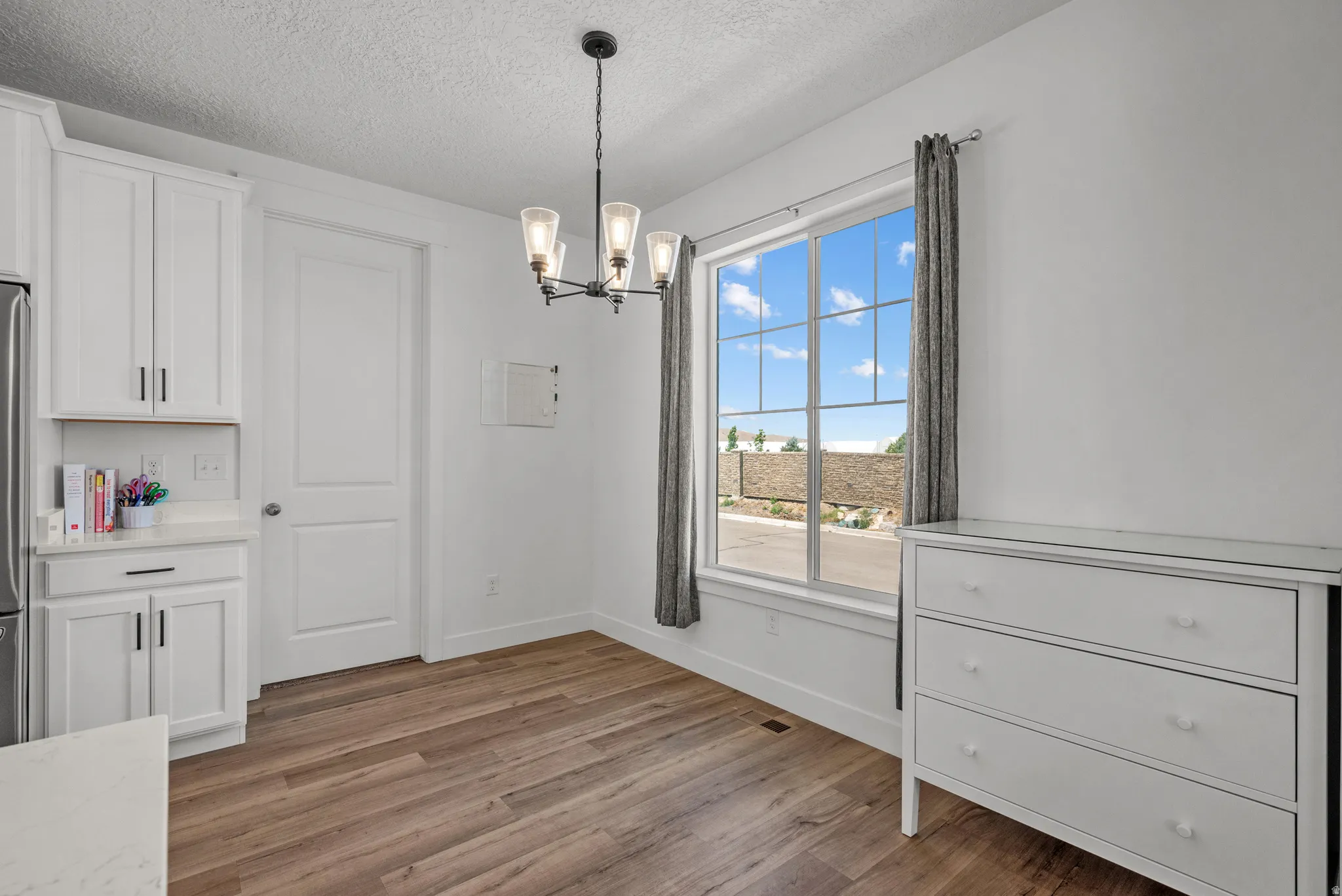 Bright interior featuring wood-finish flooring, white cabinetry with dark hardware, a large window with grid pattern, and a black chandelier with glass shades