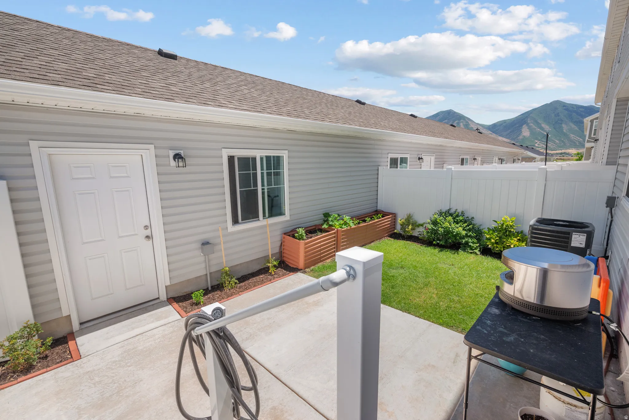 Concrete patio area with a privacy fence, a manicured lawn, and raised garden beds