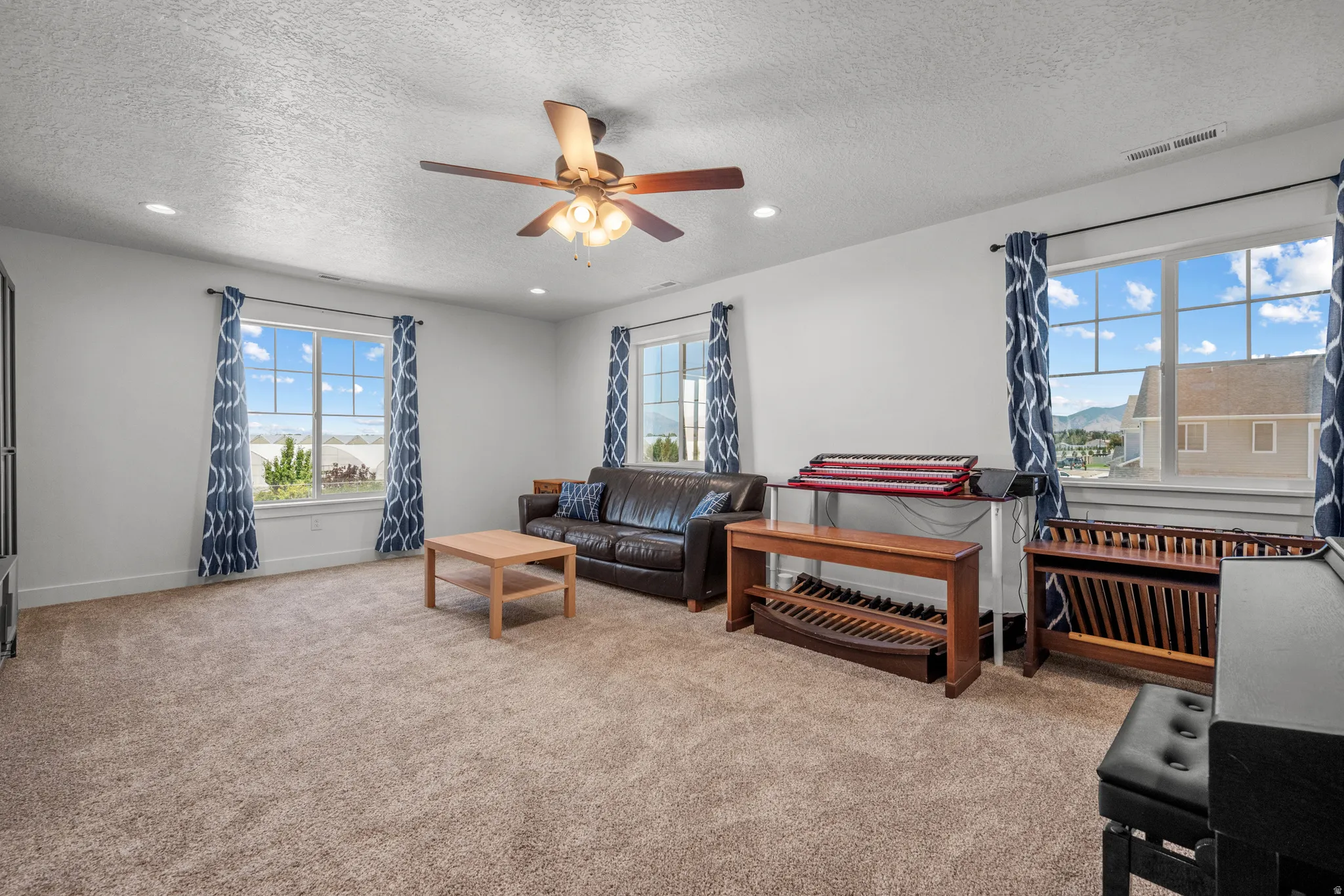 Carpeted room featuring multiple windows with patterned drapes, a ceiling fan with integrated lighting, and recessed lighting