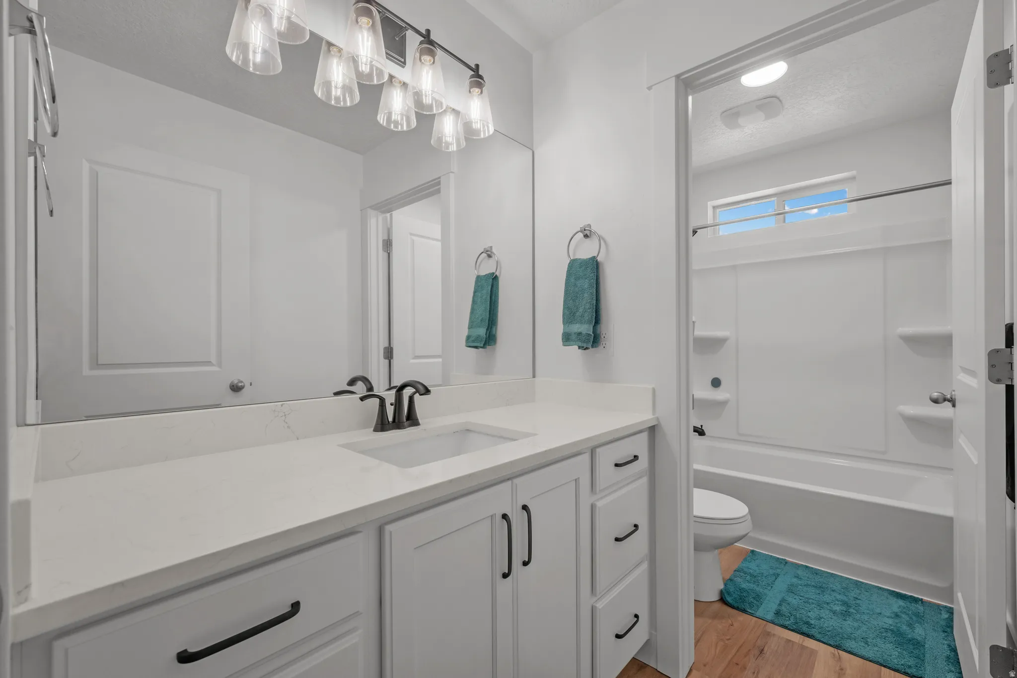 Bathroom featuring a wide vanity with a solid surface countertop and undermount sink, shaker-style cabinetry with matte black hardware, and a framed mirror with a modern light fixture