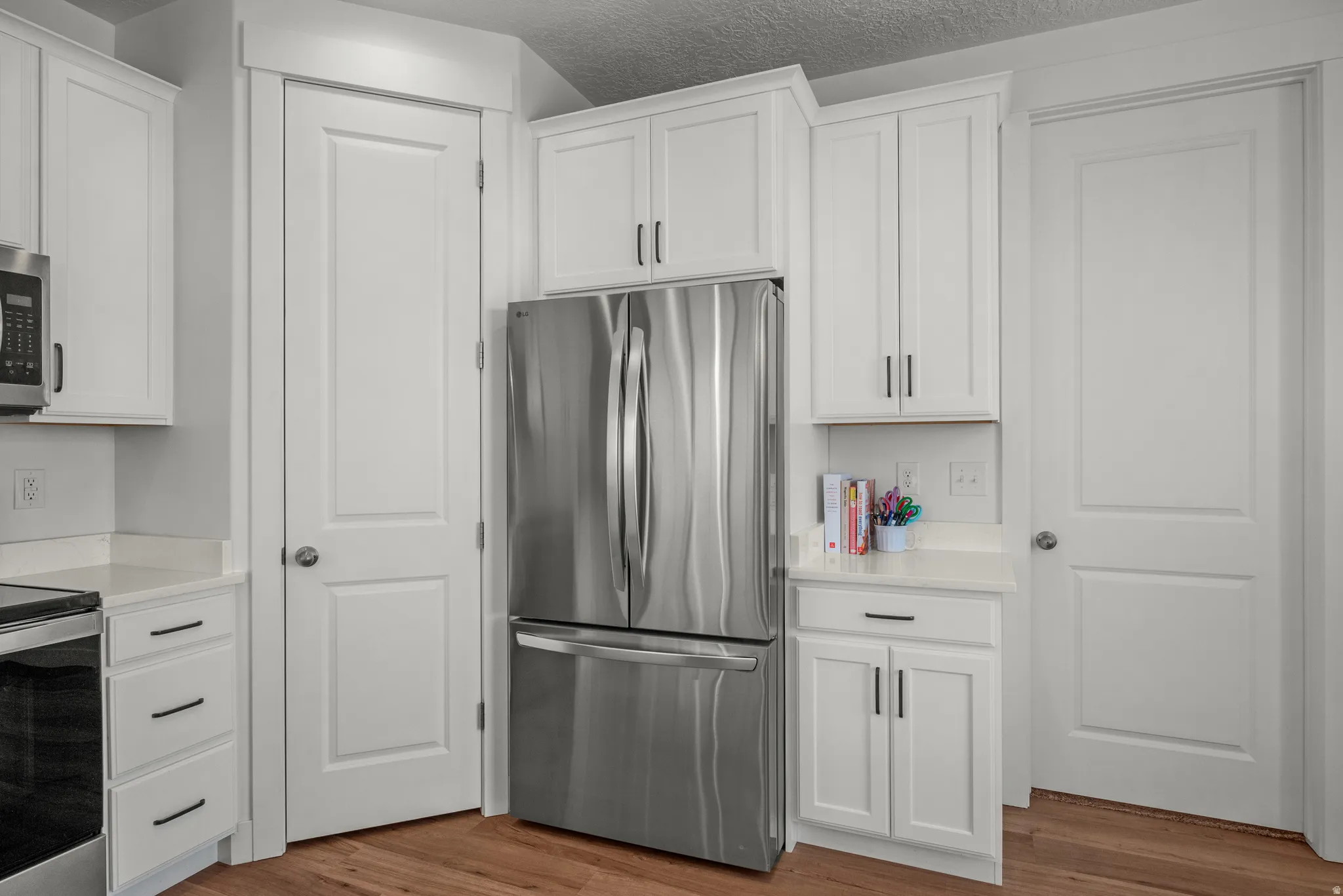 Modern kitchen featuring white shaker cabinetry with dark hardware, stainless steel refrigerator, and light countertops