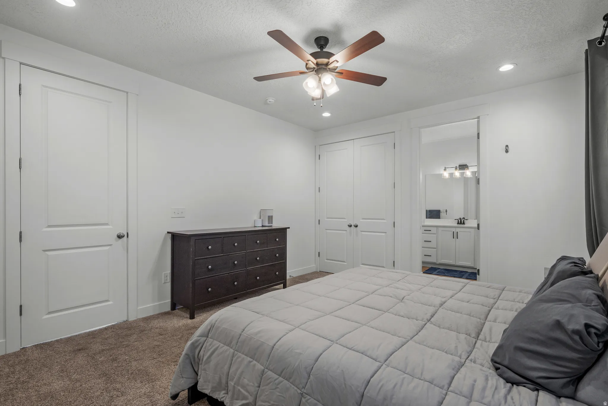 Bedroom featuring a ceiling fan, recessed lighting, carpet flooring, and a sliding door entrance to a bathroom with a vanity