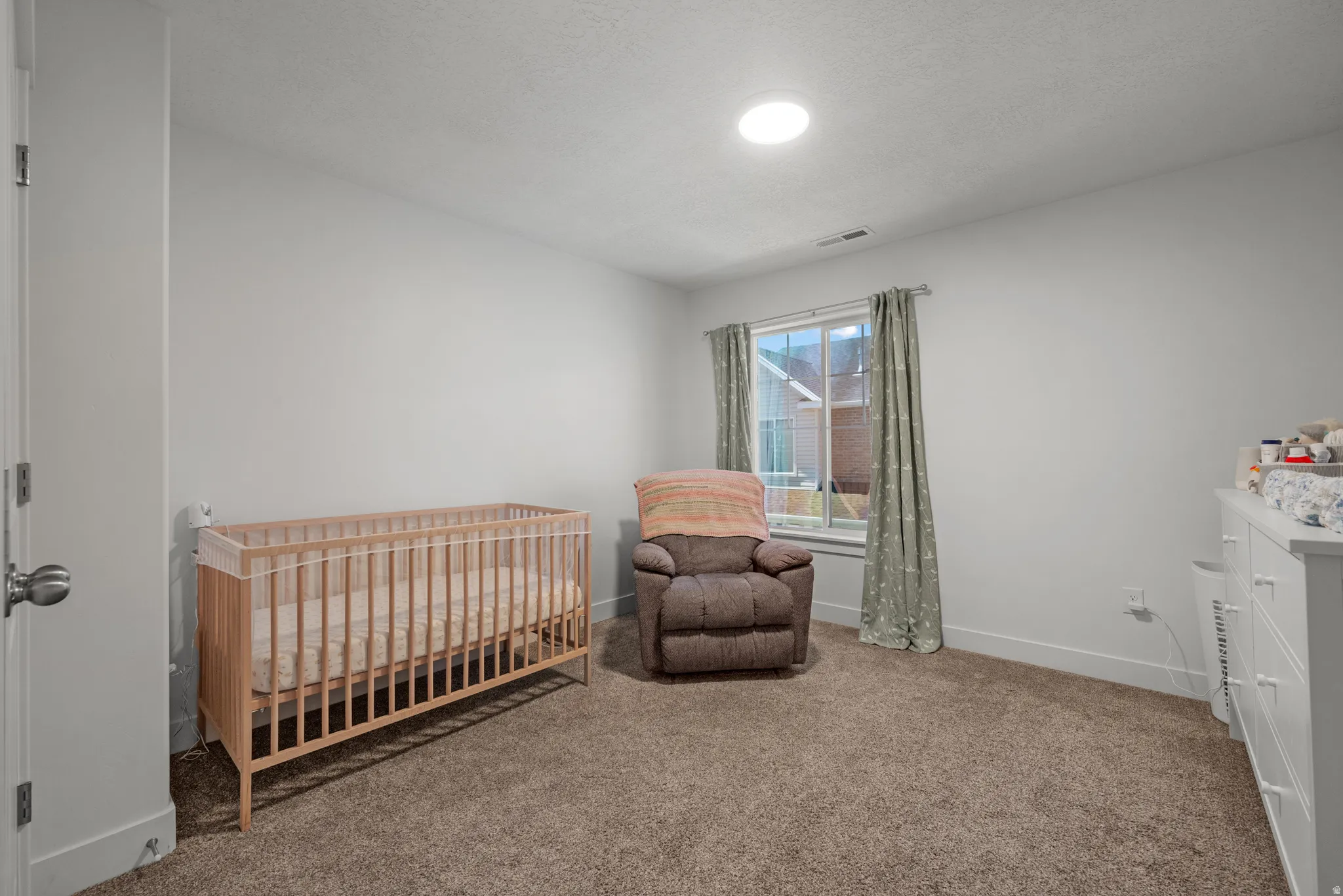 Carpeted room featuring a window with natural light, a ceiling-mounted light fixture, white walls, and white trim