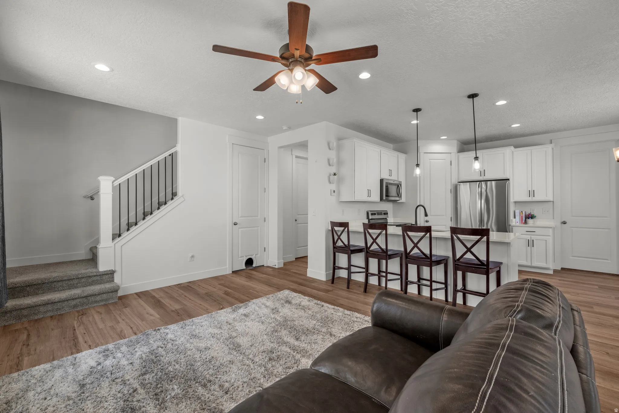 Open-concept living area featuring wood-finish flooring, a contemporary kitchen with white cabinetry, stainless steel appliances, and a central island with pendant lighting