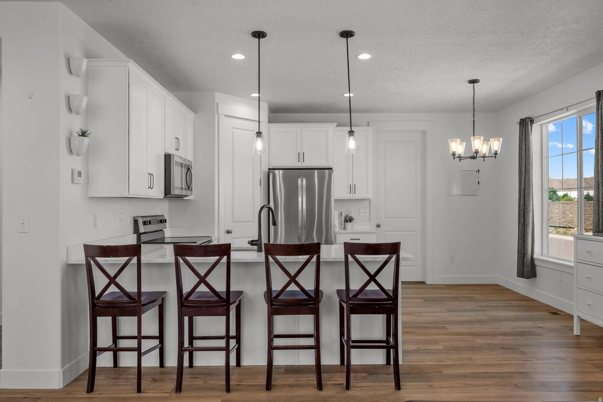 Kitchen featuring a breakfast bar with pendant lighting, white cabinetry, stainless steel appliances, and wood-finish flooring
