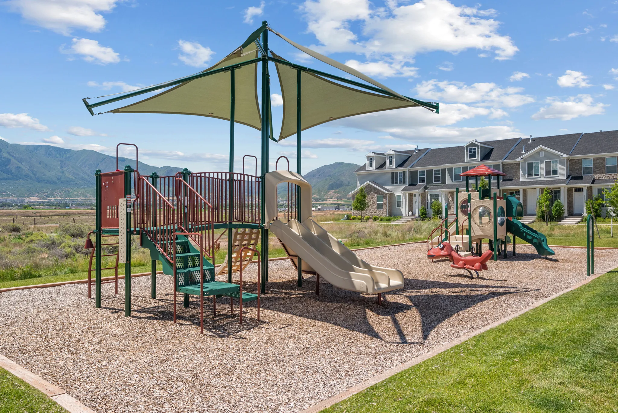 Community playground featuring shade structure, slides, swings, and climbing elements on wood chip surfacing