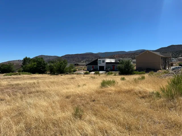 Expansive undeveloped lot featuring natural vegetation and distant mountain ranges under a clear sky