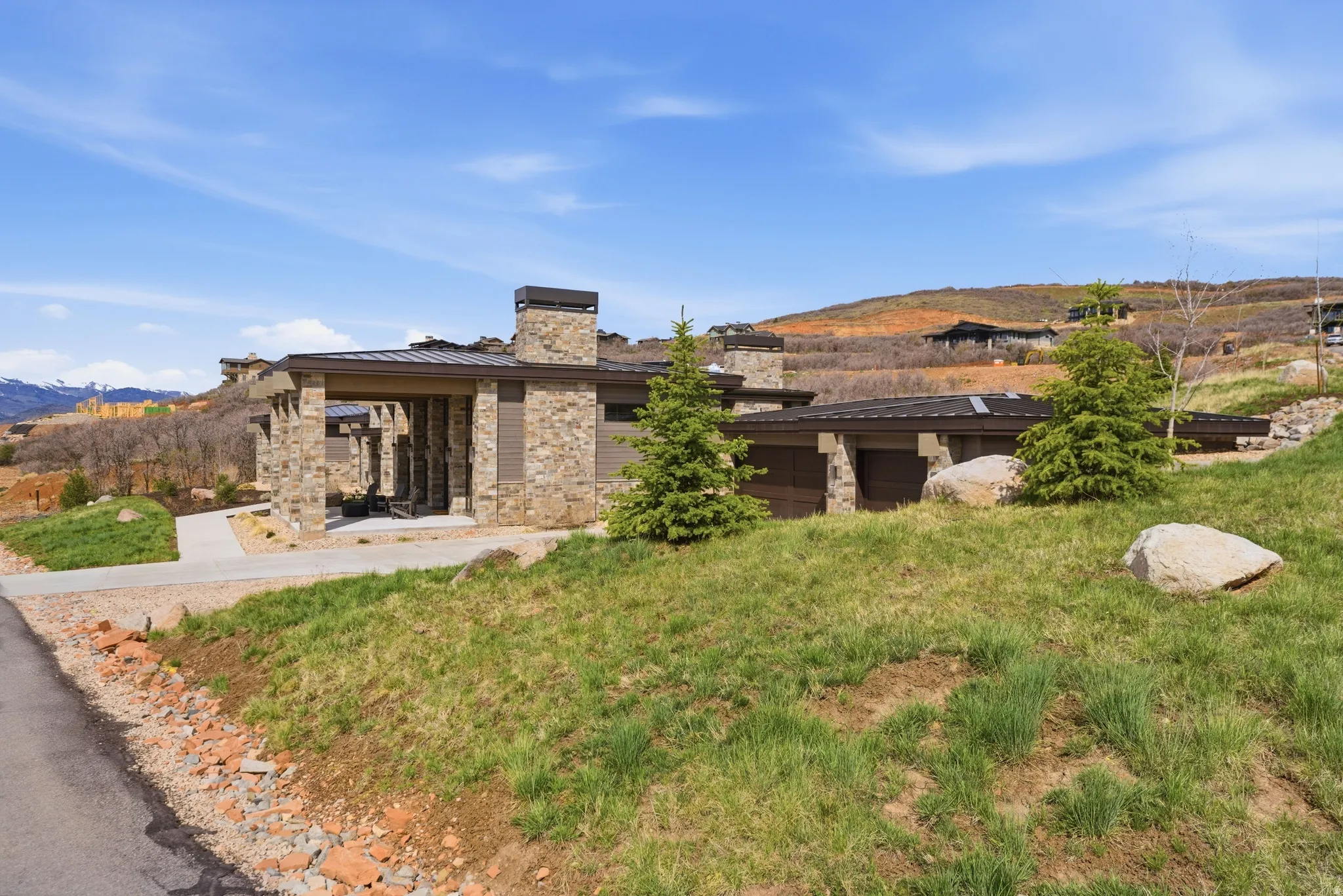 Stone and siding exterior with multiple garage bays, a paved driveway, and mature landscaping