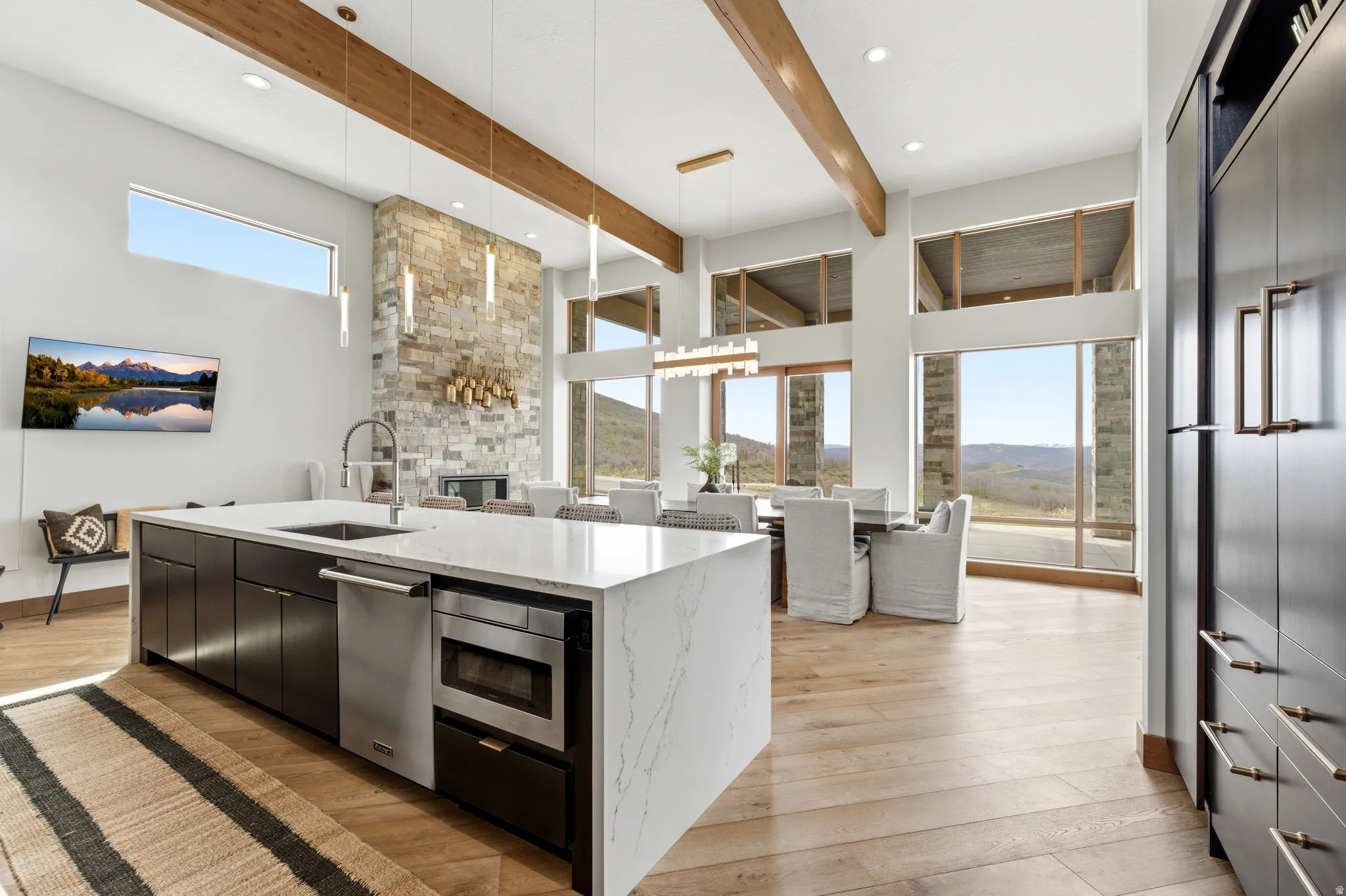 Open-concept living space featuring high ceilings with exposed wood beams, expansive floor-to-ceiling windows, and wood-finish flooring