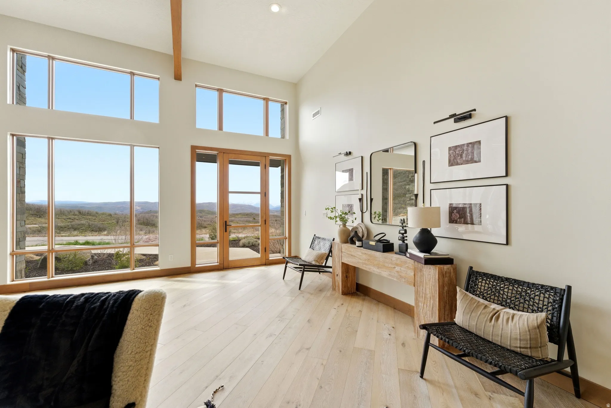 Vaulted ceiling with exposed wood beam, expansive window array, light wood-finish flooring, and double glass-panel doors