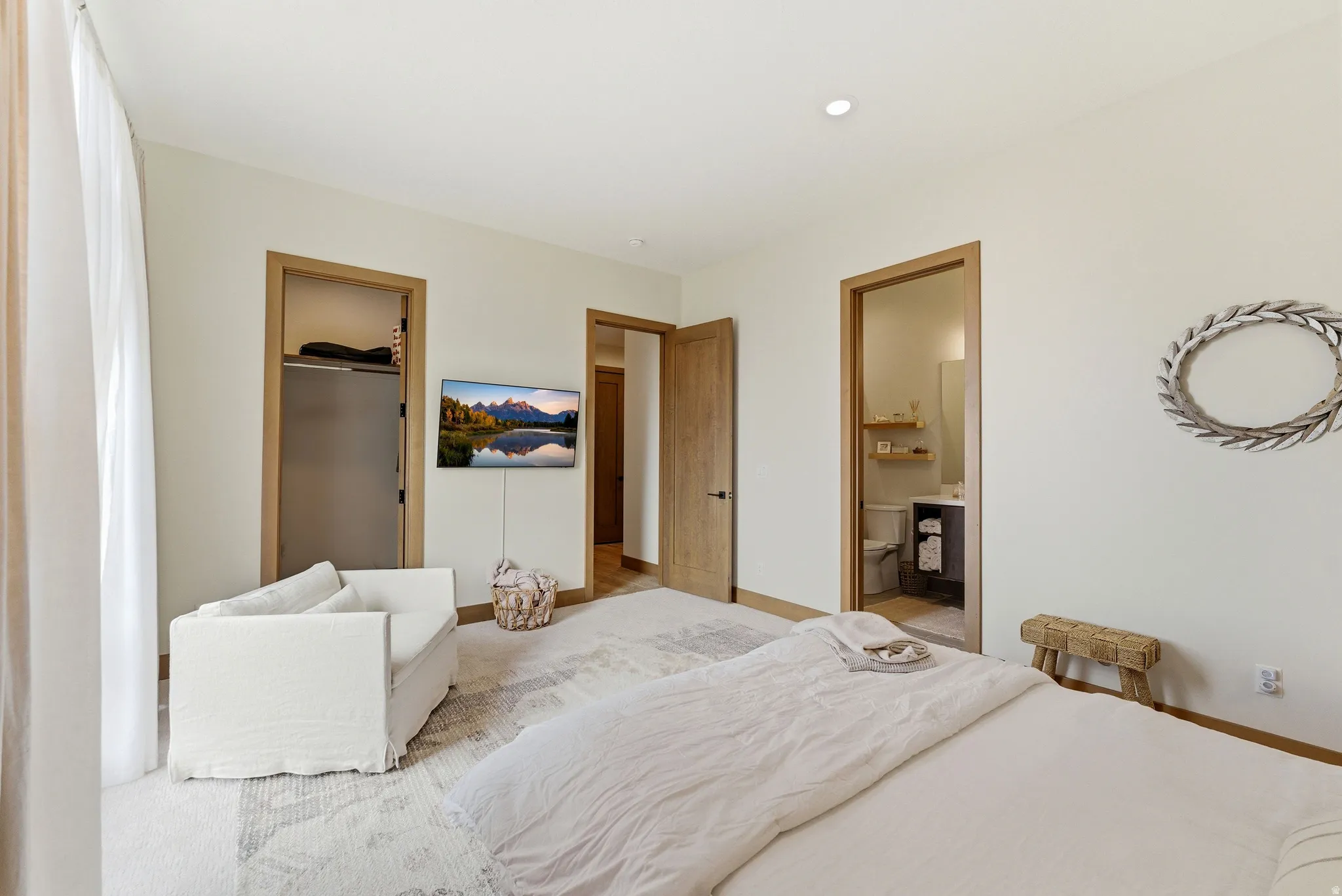 Spacious bedroom featuring light-toned walls, recessed lighting, and wood-finish door frames