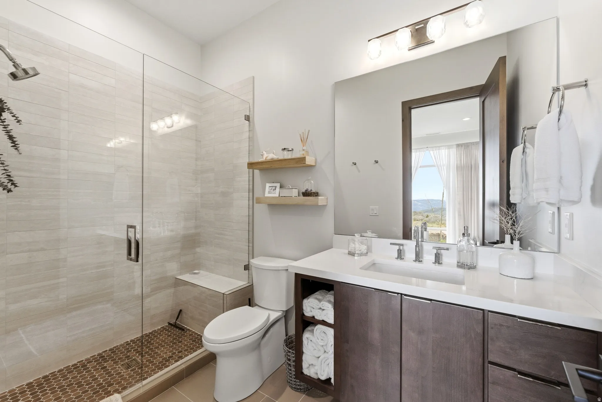 Contemporary bathroom featuring a glass-enclosed shower with a built-in bench, light-toned tile walls, and a pebble-finish floor