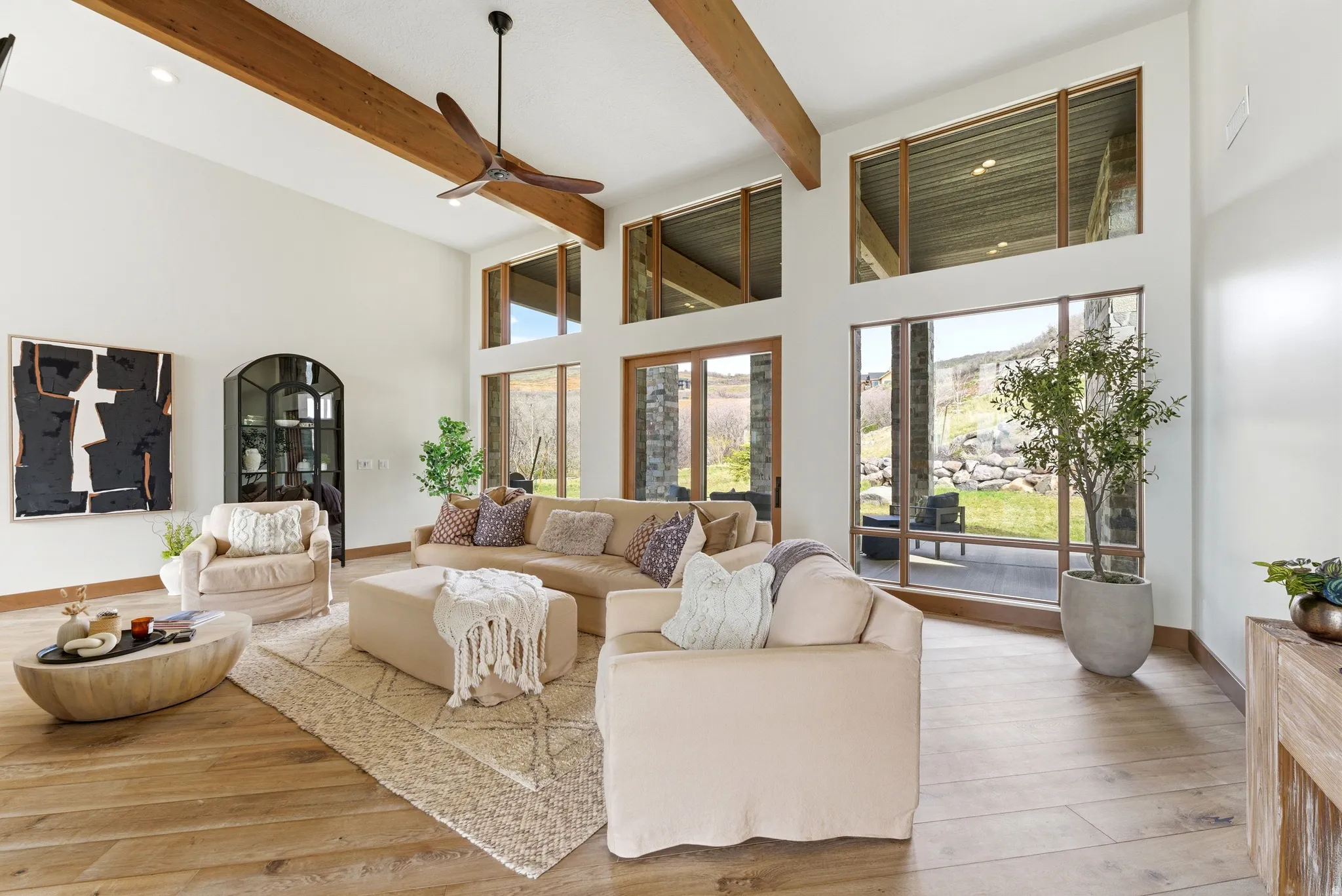 Spacious living area featuring high ceilings with exposed wood beams, extensive floor-to-ceiling windows, and wood-finish flooring