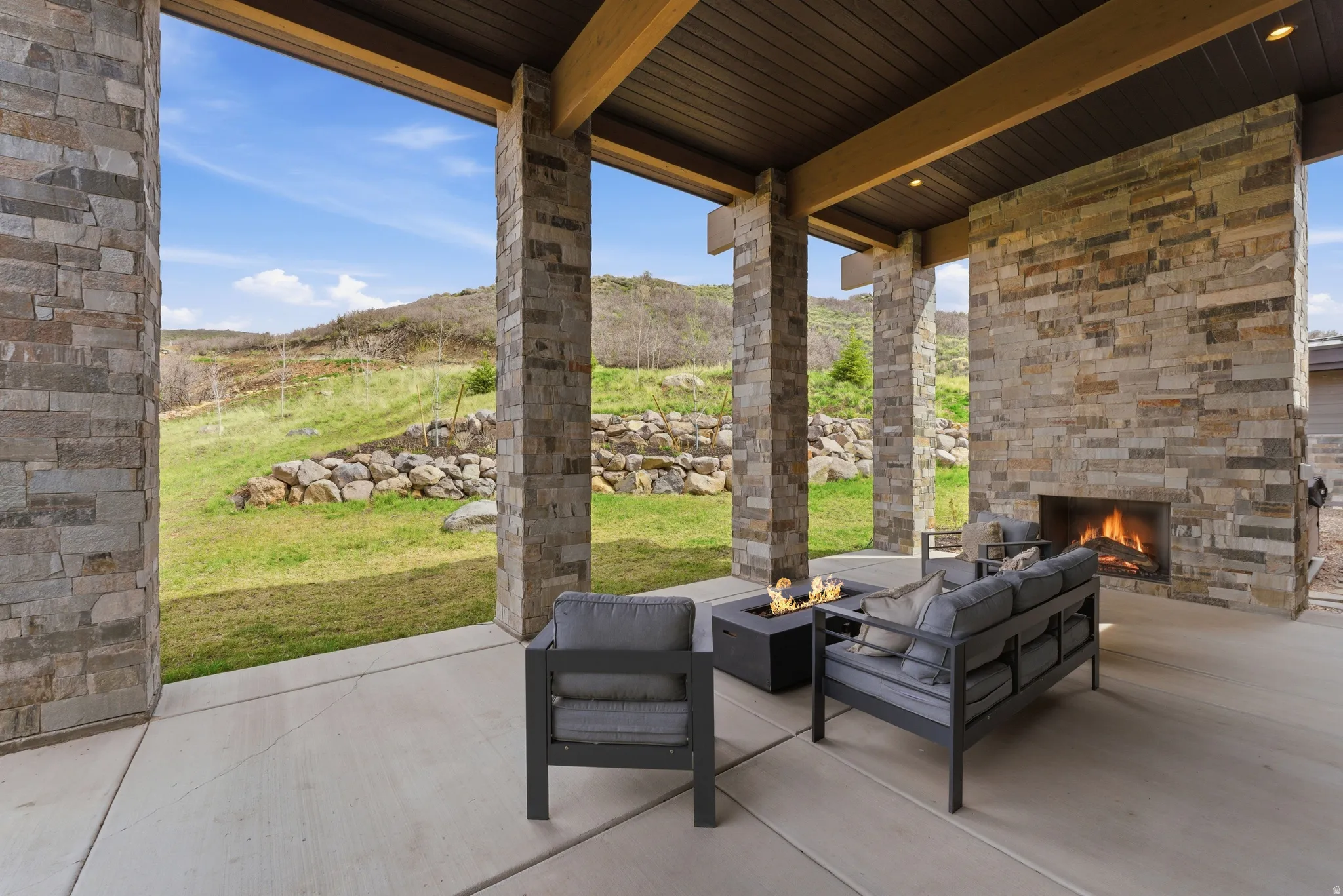 Expansive covered patio featuring a stone-clad fireplace and exposed beam ceiling