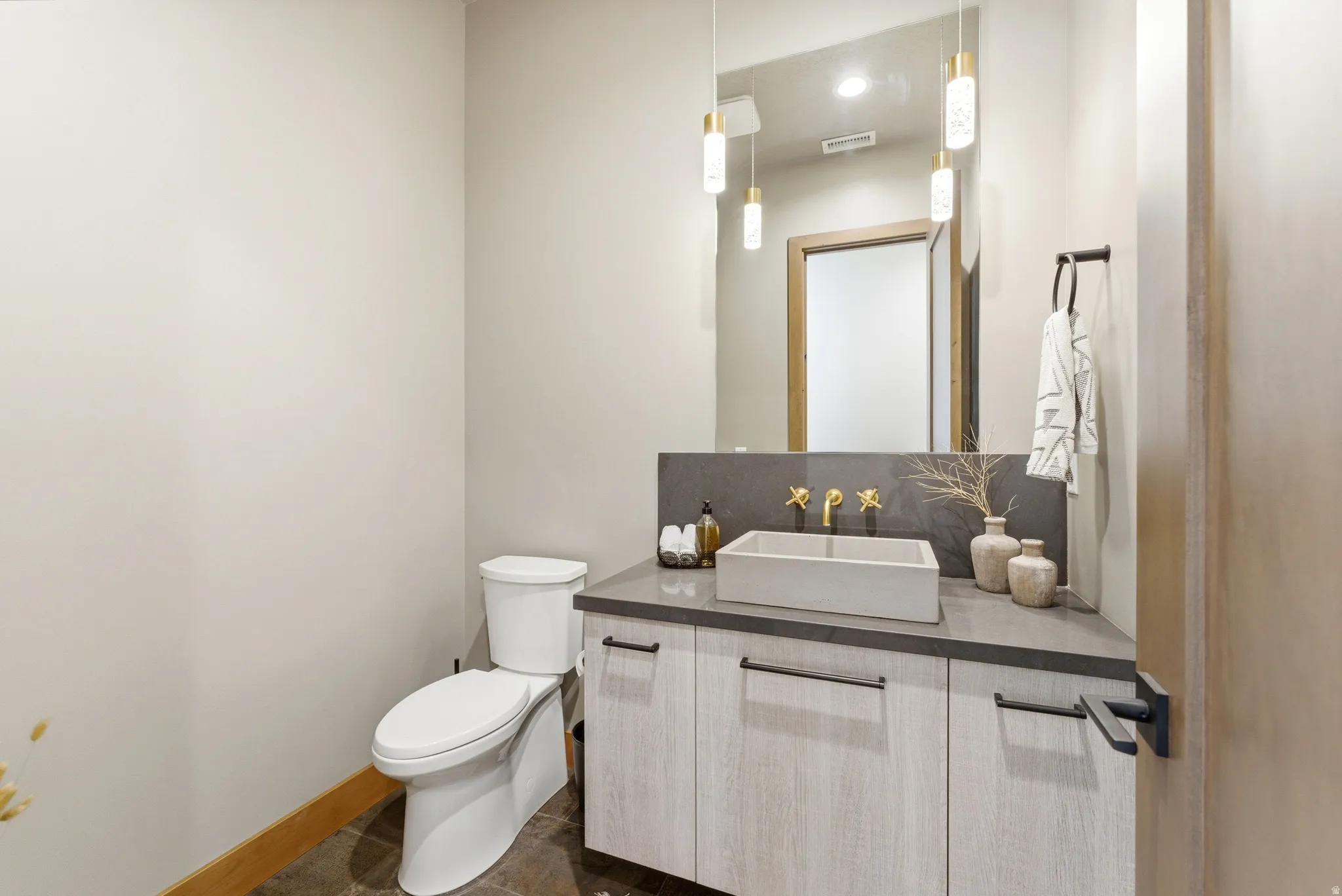 Powder room featuring a stone vanity countertop, light wood-finish cabinetry, a vessel sink with a wall-mounted faucet, and a large mirror with pendant lighting