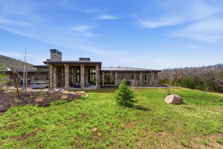 Stone-clad exterior featuring a prominent chimney, large glass panels, and a covered patio