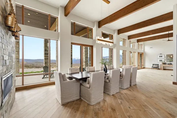 Expansive great room featuring a stone-clad fireplace with an integrated firebox, floor-to-ceiling windows, exposed wood ceiling beams, and wide plank wood-finish flooring