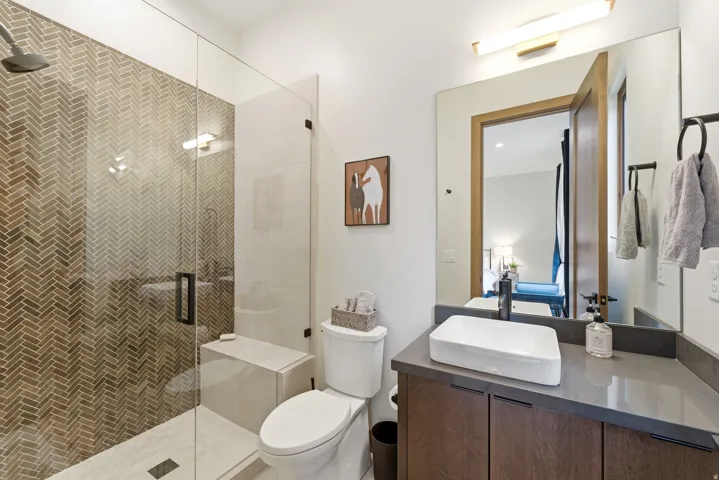 Bathroom featuring a glass-enclosed shower with herringbone tile, a built-in shower bench, a modern floating vanity with a vessel sink, a dark countertop, and a large wall mirror