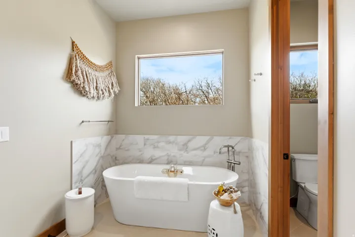 Freestanding soaking tub with a floor-mounted faucet, complemented by marble-finish wall tiling and a rectangular window