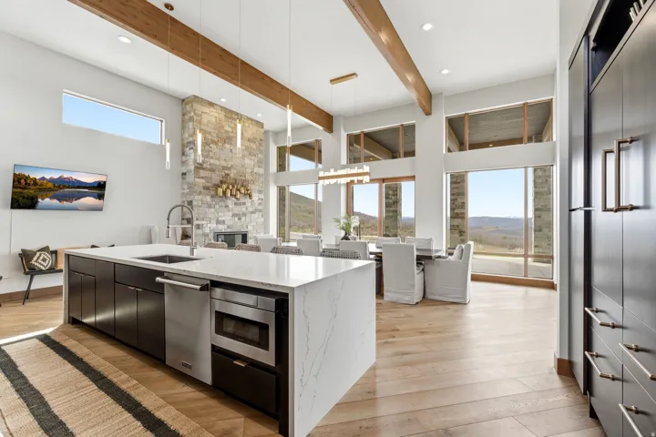 Open-concept living space featuring high ceilings with exposed wood beams, expansive floor-to-ceiling windows, and wood-finish flooring