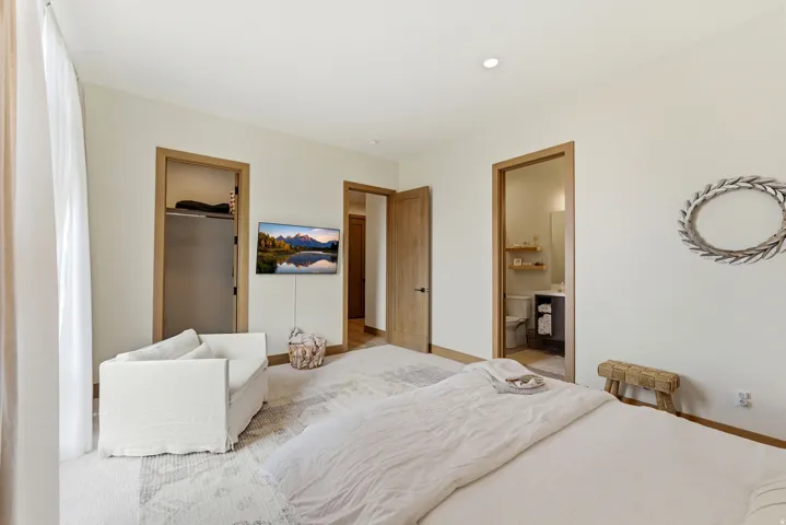 Spacious bedroom featuring light-toned walls, recessed lighting, and wood-finish door frames