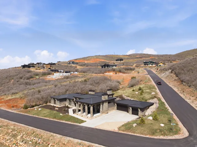 Contemporary stone and stucco exterior with a multi-car garage, black roof, and an expansive paved driveway