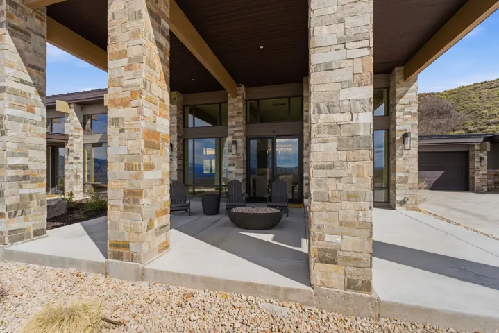 Expansive stone exterior featuring a covered patio, integrated garage, large windows, and a gravel landscape