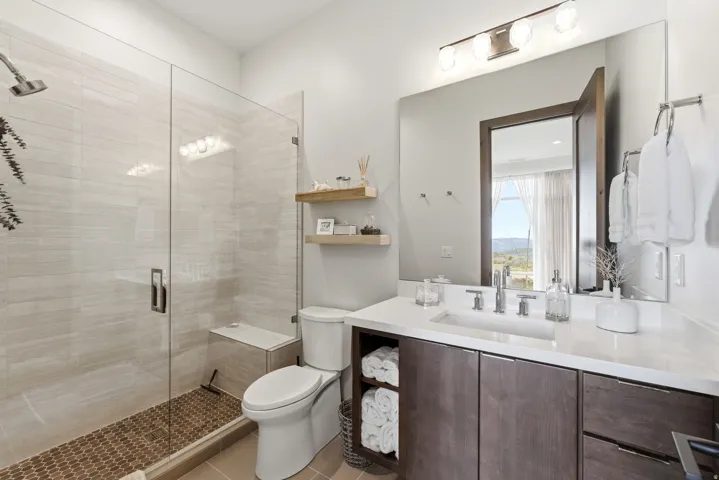 Contemporary bathroom featuring a glass-enclosed shower with a built-in bench, light-toned tile walls, and a pebble-finish floor