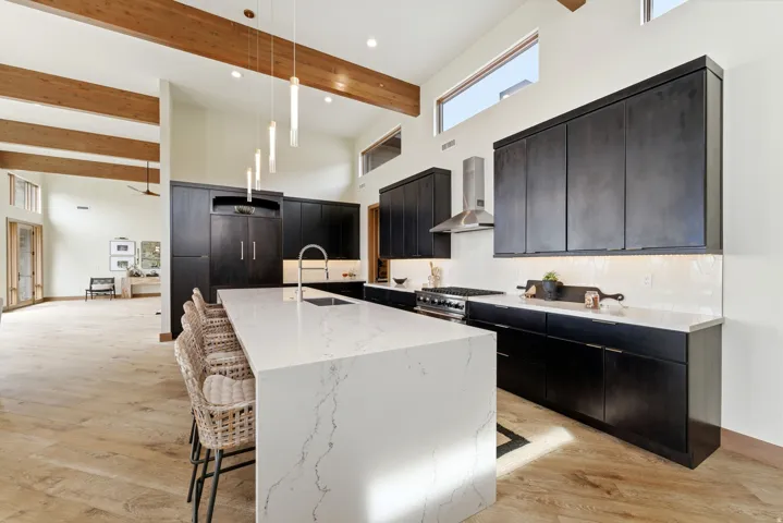 Gourmet kitchen featuring a large waterfall-edge island with seating, dark wood-finish cabinetry, stainless steel appliances, and light wood-finish flooring