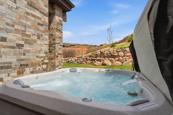 Outdoor hot tub with integrated waterfall feature, set against a stacked stone exterior