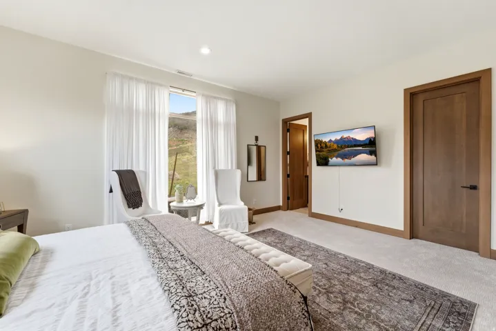 Carpeted room featuring a large window with sheer white drapery, natural wood trim and doors, and recessed lighting