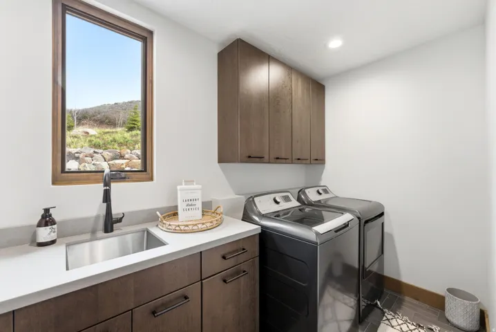 Dedicated laundry room featuring wood-finish cabinetry, a stainless steel sink with a matte black faucet, and light-toned countertops