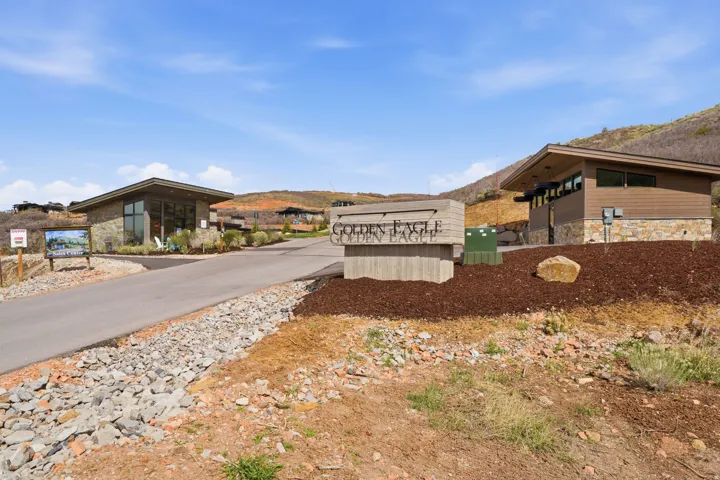 Community entrance featuring a central monument sign, stone-clad gatehouses, and paved roadways